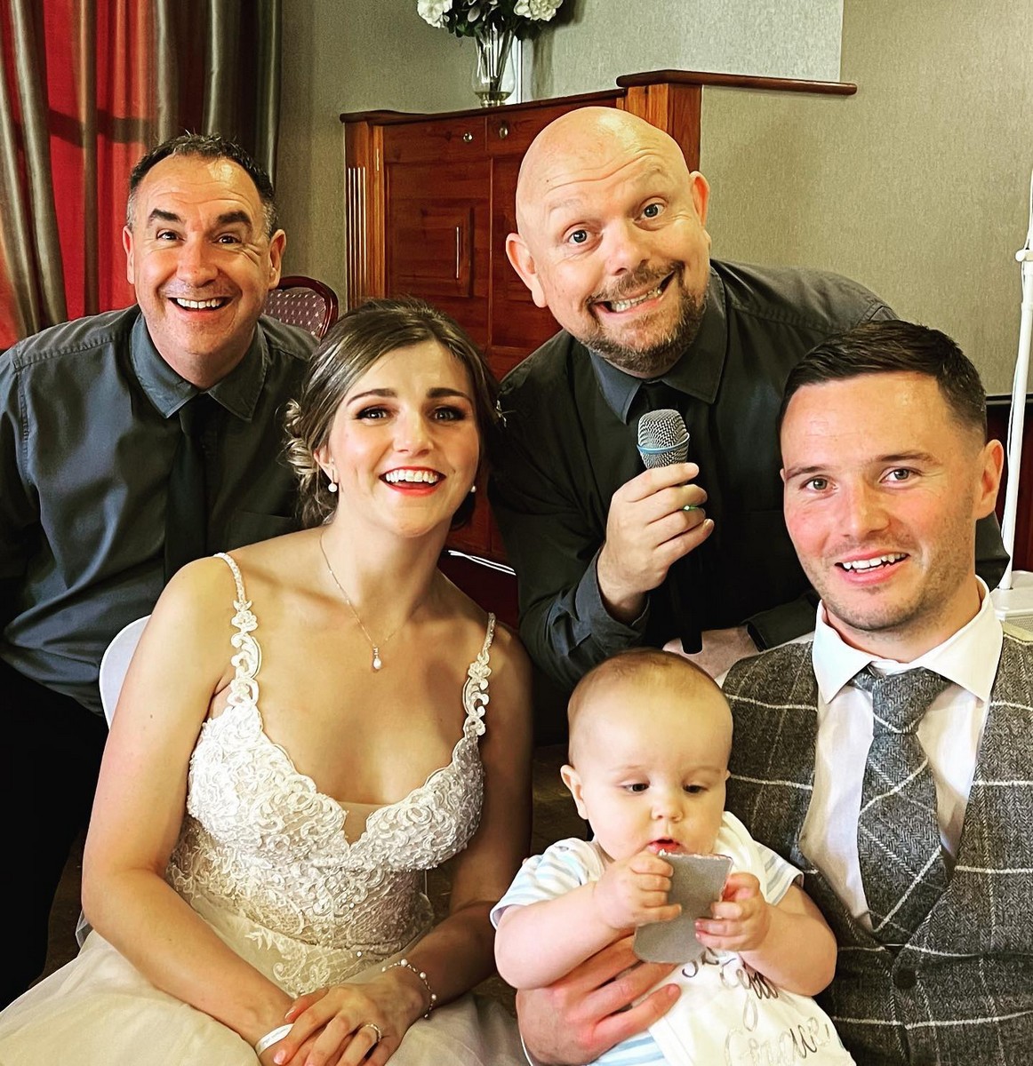 The Sing Along Waiters performing at intimate wedding reception with newlyweds and baby, award-winning singing waiters in Manchester showing family-friendly entertainment, professional performers with microphone in elegant venue setting