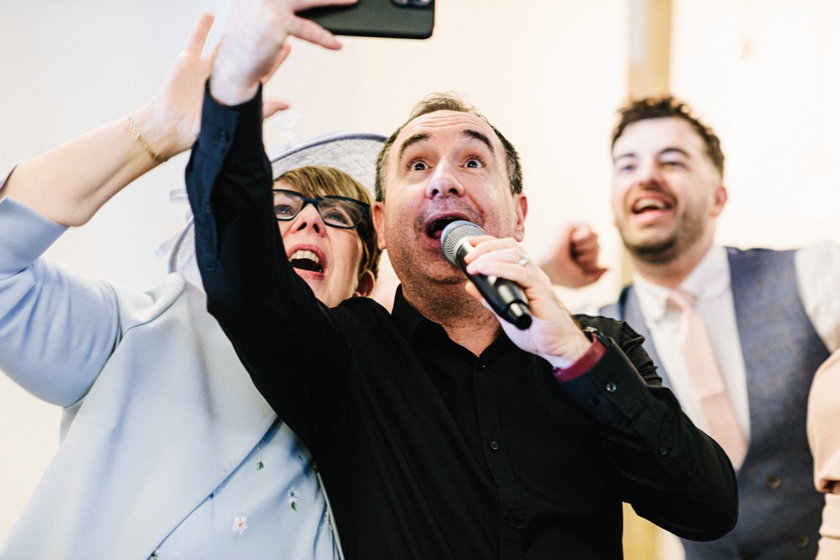 Singing waiters engaging guests by taking a group selfie during a lively performance.