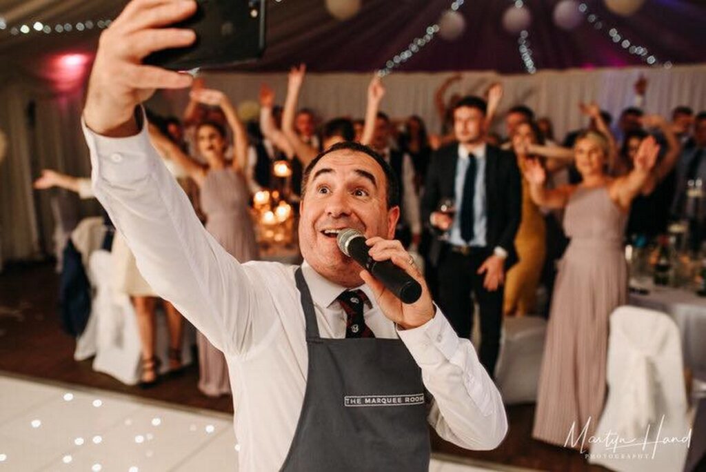 The Sing Along Waiters performing at The Marquee Room Bowden - surprise singing waiter in venue-branded apron leading interactive wedding entertainment with enthusiastic guest participation